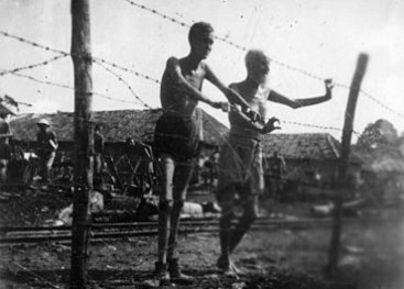 Two very skinny men standing inside a fence.